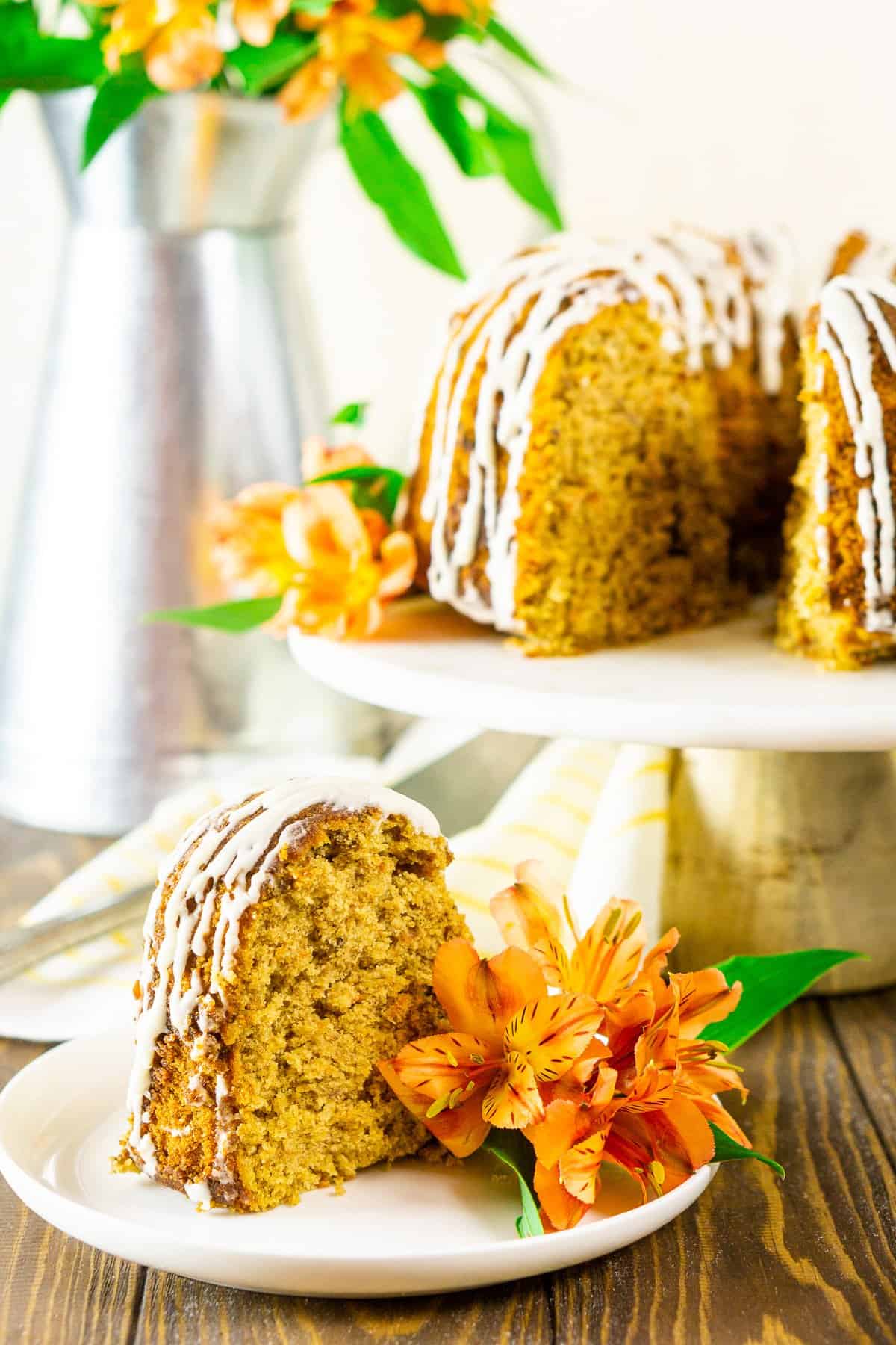 A slice of the carrot pound cake on a white plate with the rest of the cake in the background.