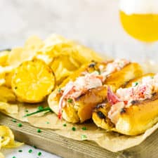 Two Maine-style lobster rolls on parchment paper with a beer in the background.