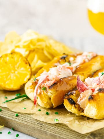 Two Maine-style lobster rolls on parchment paper with a beer in the background.