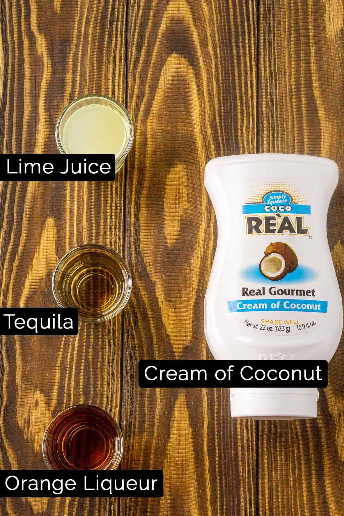 The coconut margarita ingredients with black and white labels on a wooden board.