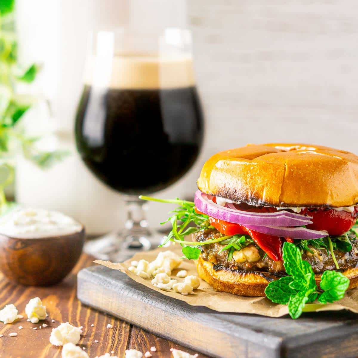 A minted lamb burger on a wooden tray with a stout in the background.