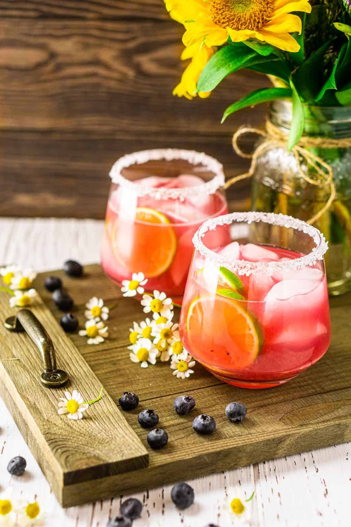 Looking down on two blueberry margaritas with flowers and blueberries around it.