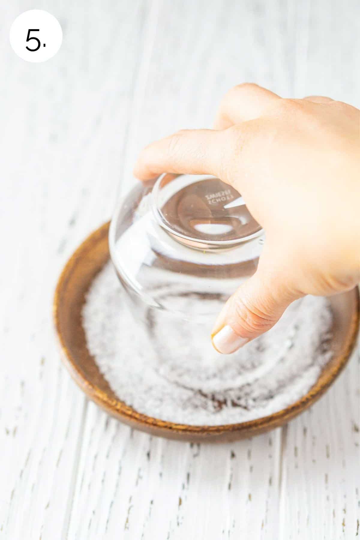 Swirling the glass in sea salt on a small wooden plate.