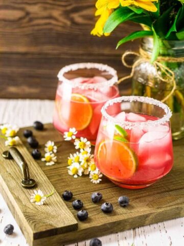 Looking down on two blueberry margaritas with flowers and blueberries around it.