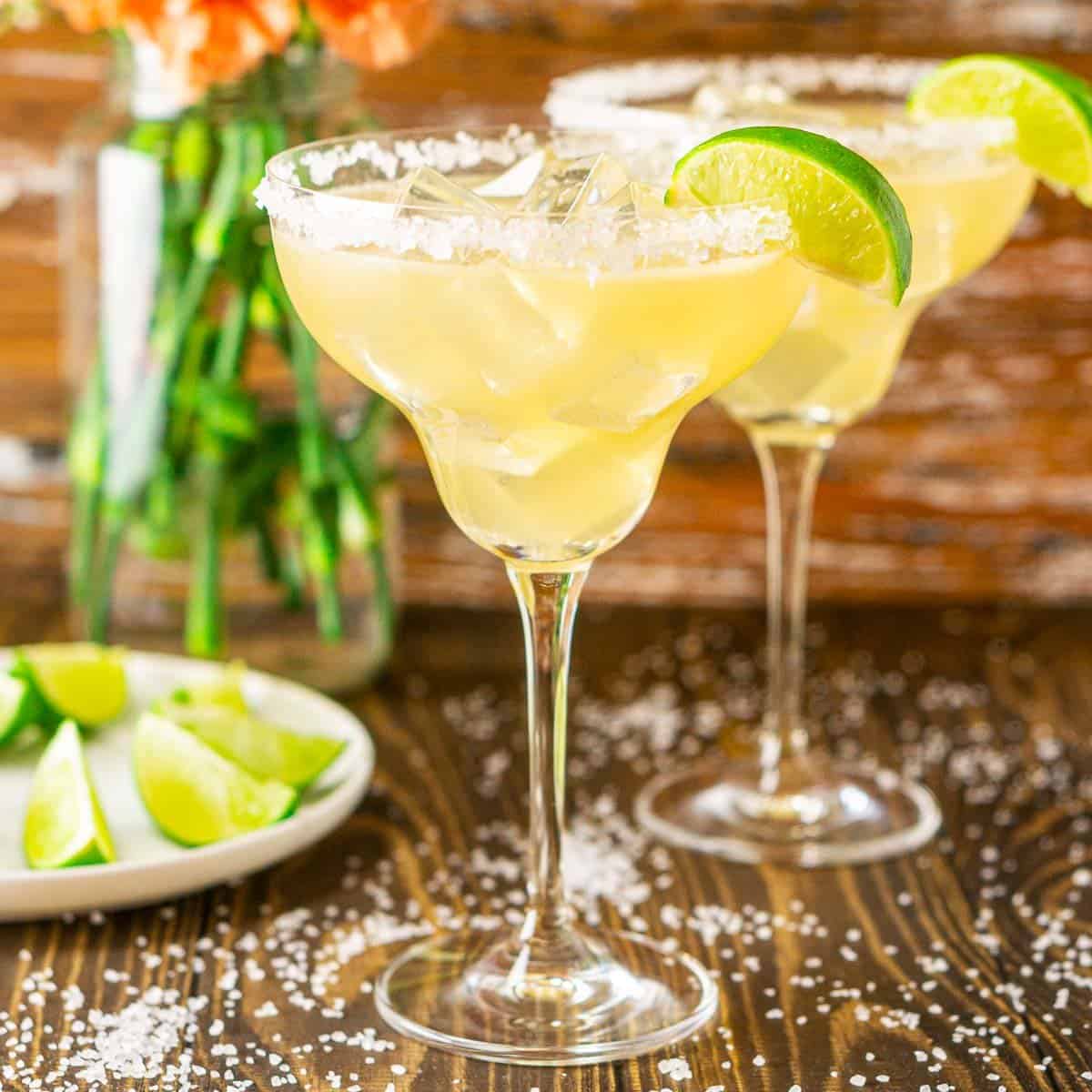 Two Cadillac margaritas with orange flowers in the background and sea salt around them.