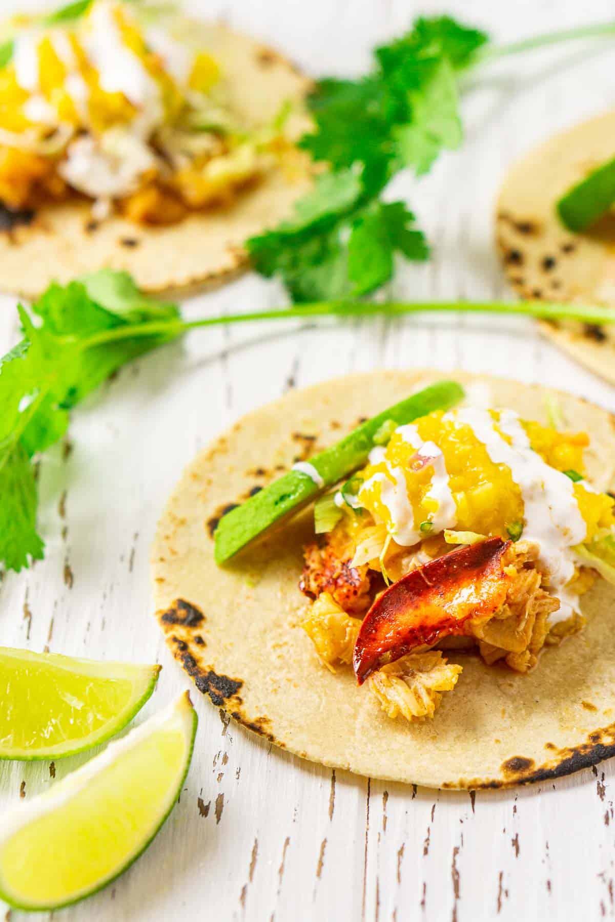 The lobster tacos on a white wooden board with limes and cilantro around it.
