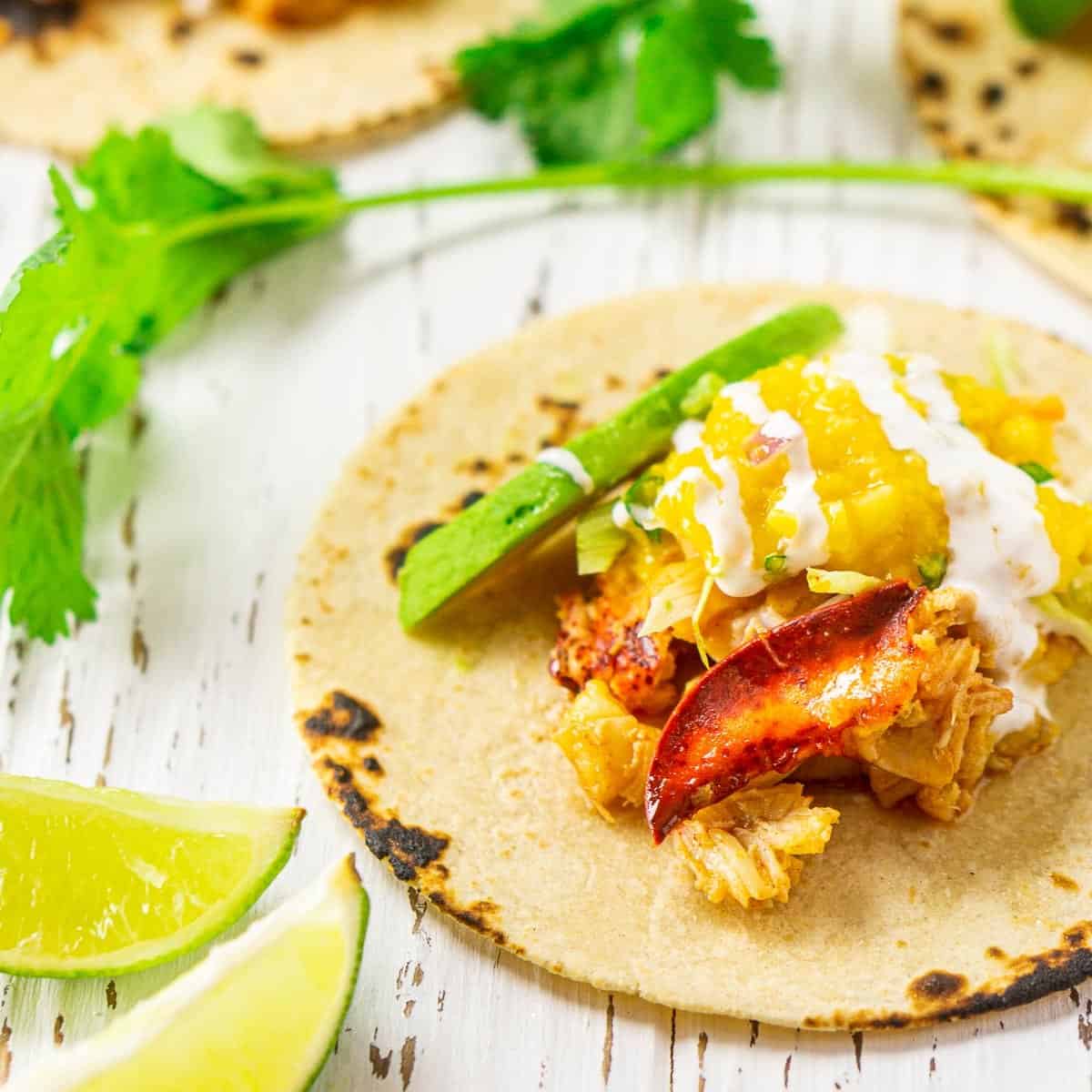 A lobster taco on a white wooden surface with lime slices to the side.