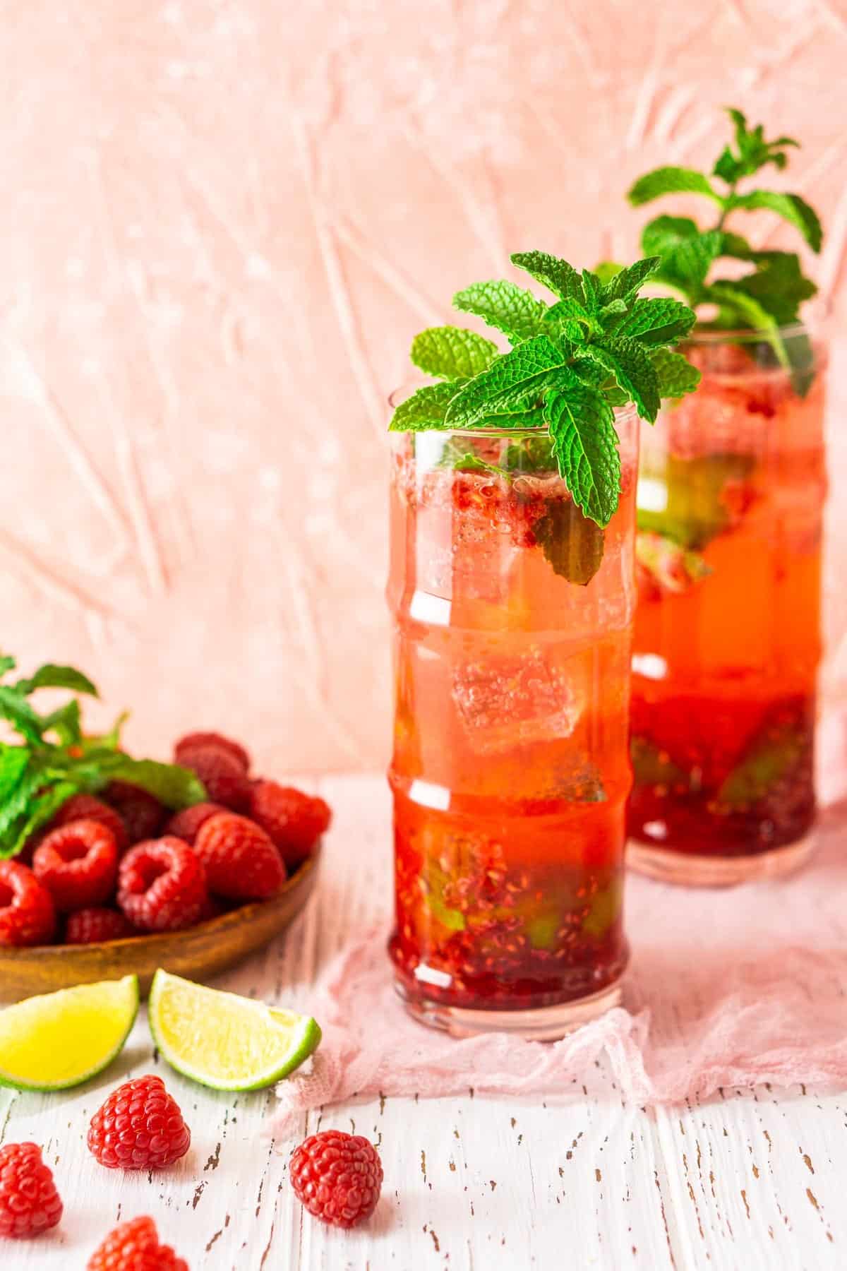 Two raspberries mojitos with limes and raspberries to the left.