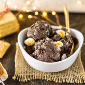 A bowl of homemade s'mores ice cream with twinkling lights and a stack of graham crackers behind it.