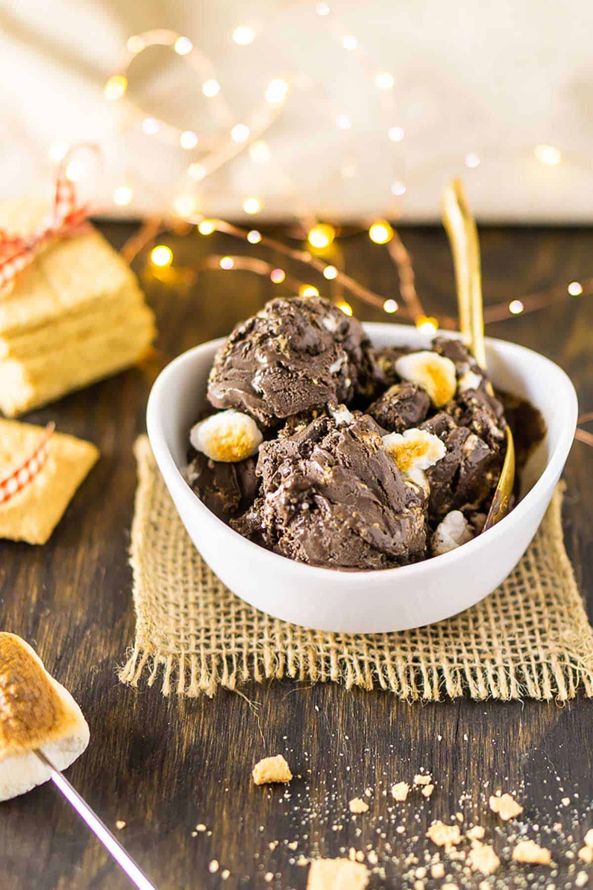 A bowl of homemade s'mores ice cream with twinkling lights and a stack of graham crackers behind it.