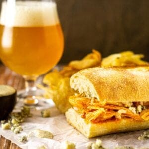 A Buffalo chicken sub with a beer next to it and blue cheese crumbles around it.