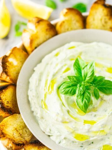 A bowl of whipped ricotta dip with grilled bread around it.