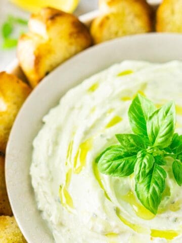 A bowl of whipped ricotta dip with grilled bread to the side and fresh lemon slices in the background.