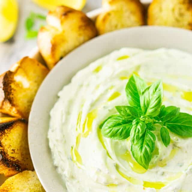 A bowl of whipped ricotta dip with grilled bread to the side and fresh lemon slices in the background.