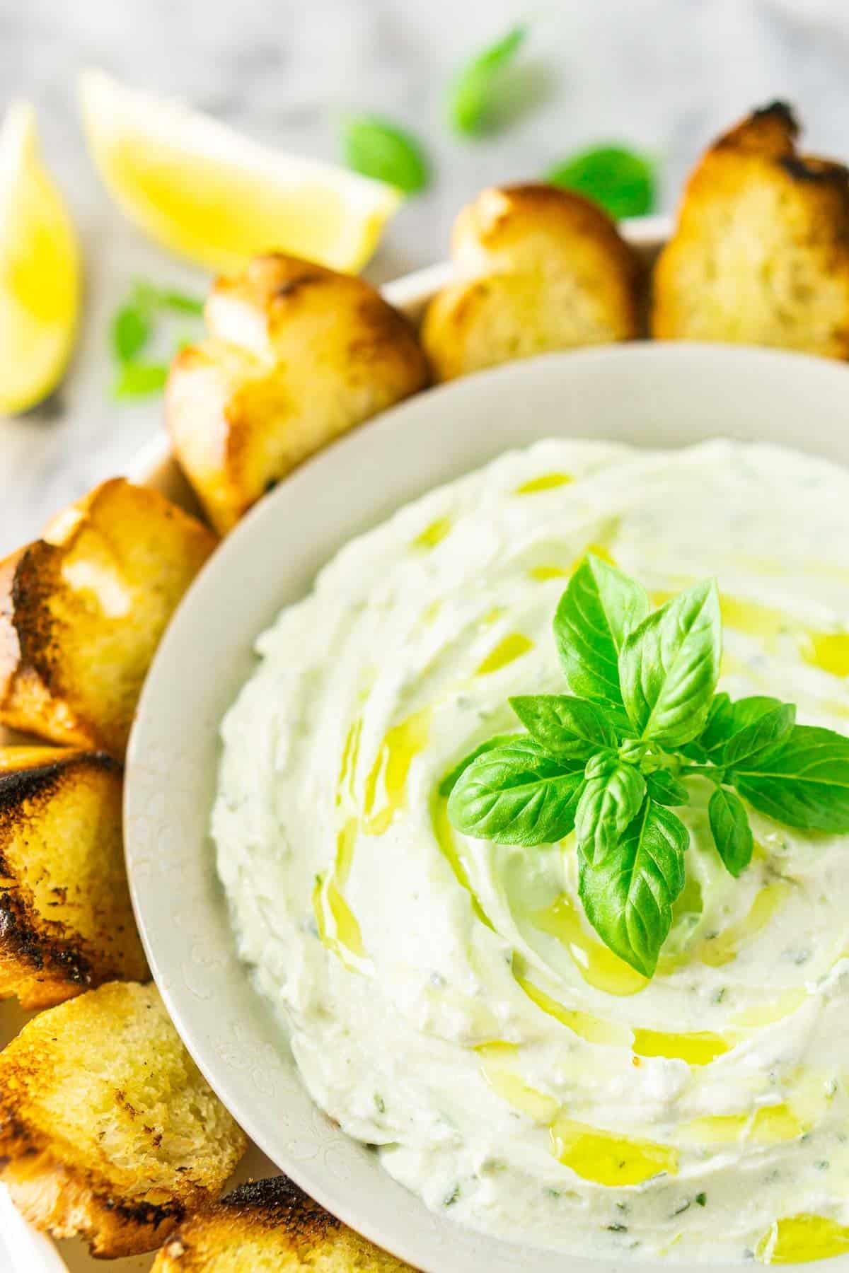 A bowl of whipped ricotta dip with grilled bread to the side and fresh lemon slices in the background.