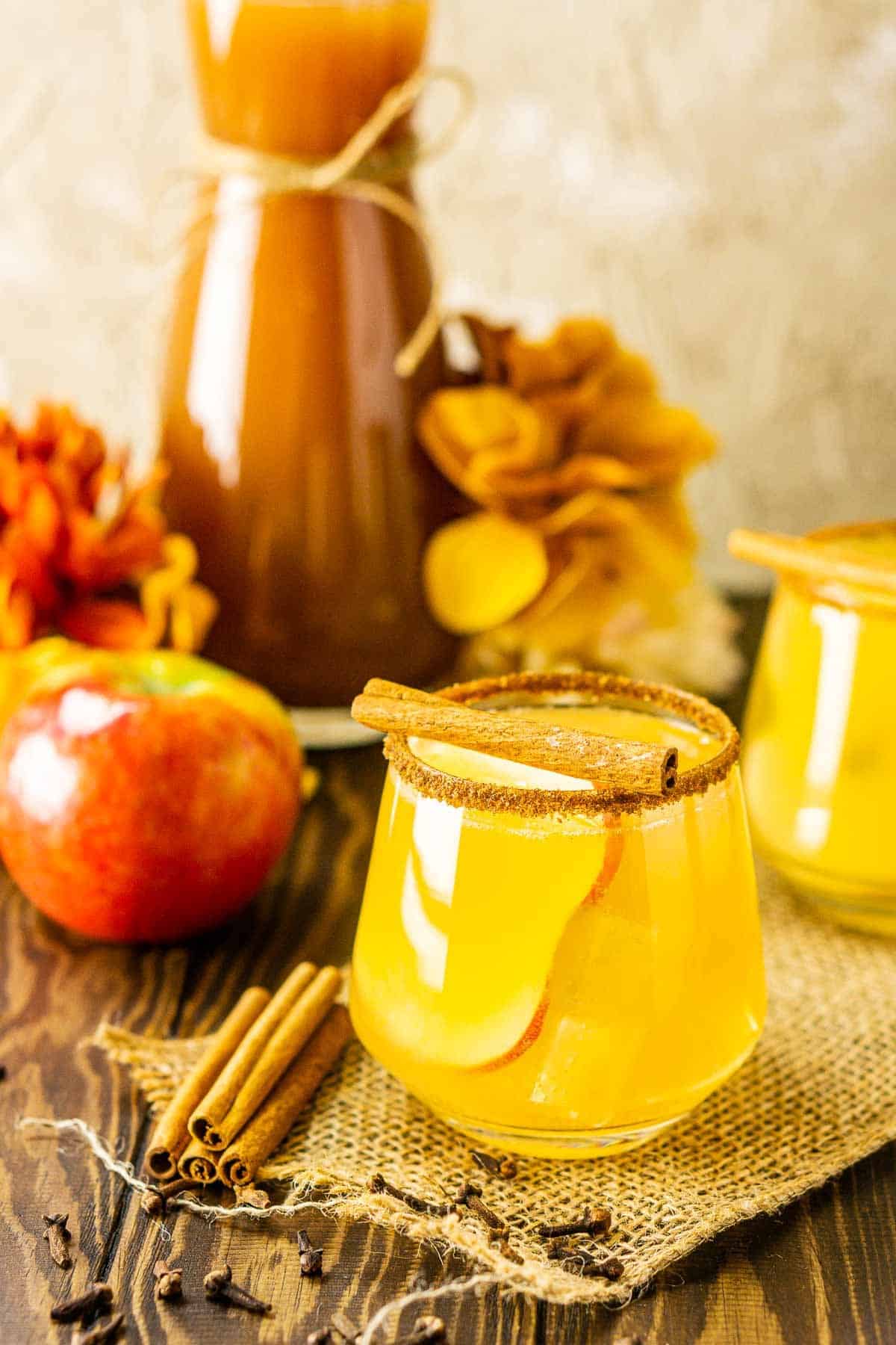 A sparkling apple cider margarita with cinnamon sticks and an apple to the side.