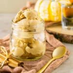 A mason jar full of bourbon pumpkin ice cream with a gold spoon to the side and a bundle of cinnamon sticks.