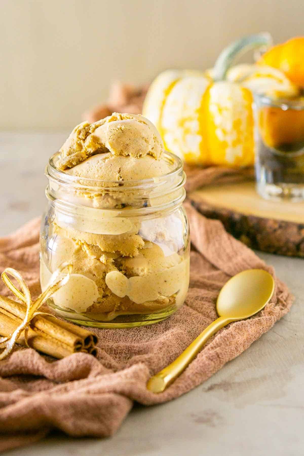 A mason jar full of bourbon pumpkin ice cream with a gold spoon to the side and a bundle of cinnamon sticks.