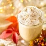A maple latte on sweater material with fall flowers and lights by it.