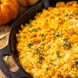 A cast-iron skillet filled with pumpkin mac and cheese on burlap with sage next to it.