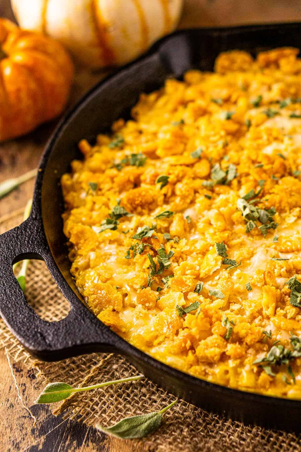 A cast-iron skillet filled with pumpkin mac and cheese on burlap with sage next to it.