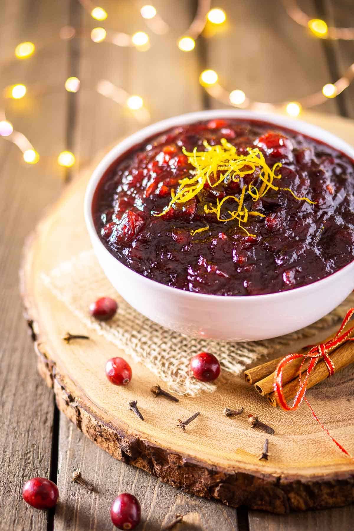 A bowl of spiced-brandied cranberry sauce on a wooden platter with cranberries and spices around it.