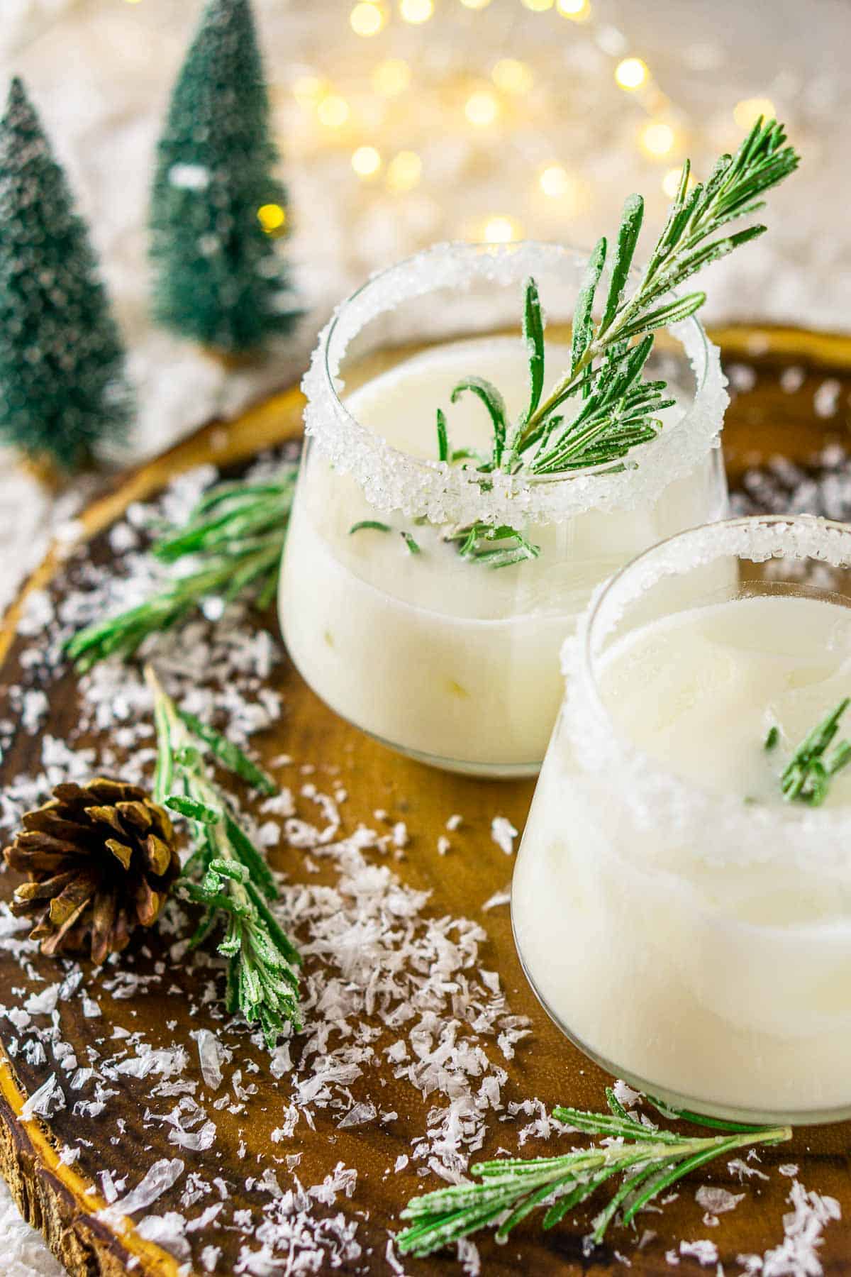 A festive Christmas cocktail on a wooden platter with fake snow and pine trees around it.
