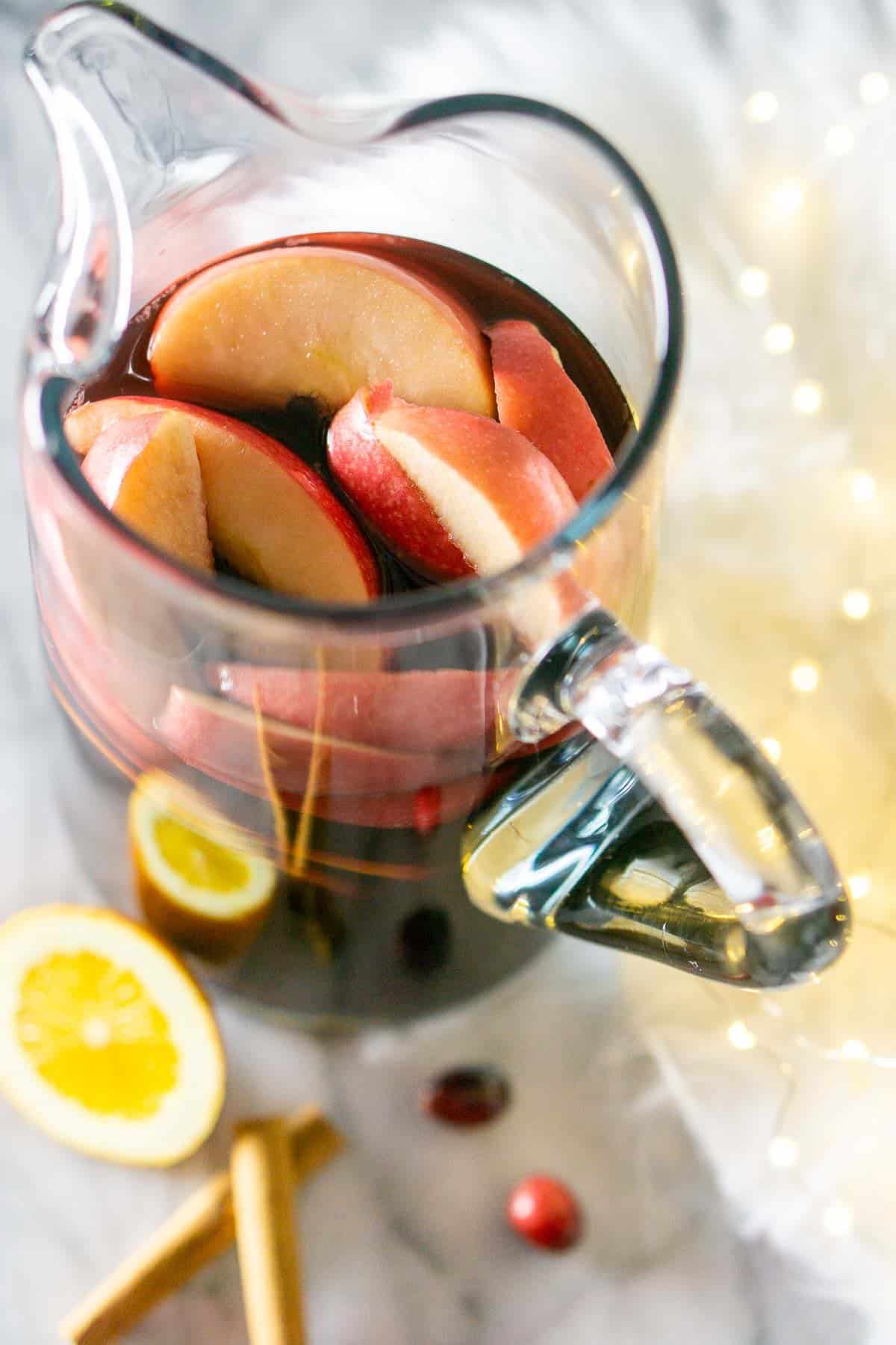 A pitcher of holiday sangria with fresh cranberries and cinnamon sticks to the side.