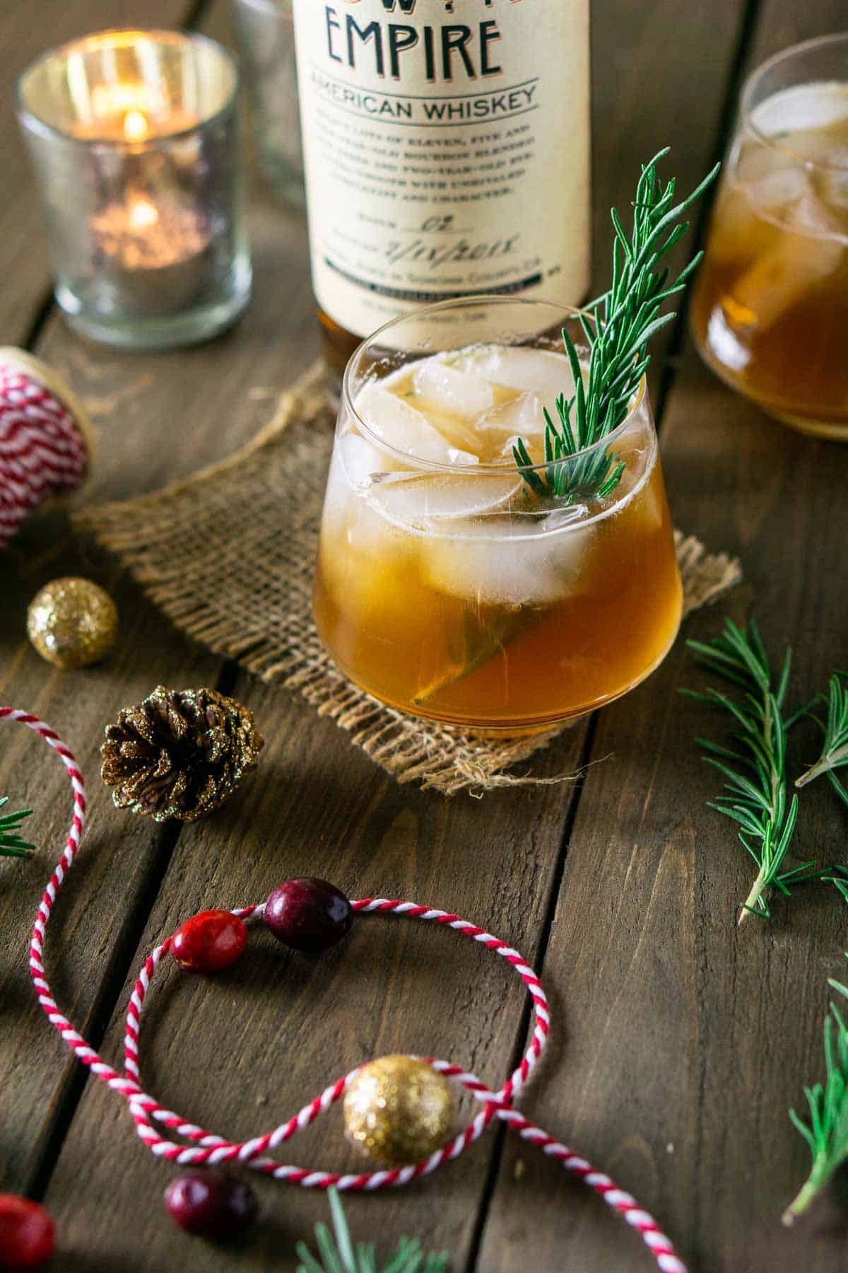 A bourbon holiday cocktail with Christmas decor and candles around it.