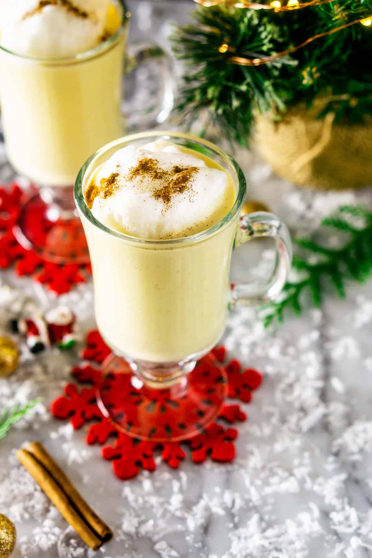 A glass of maple eggnog with a Christmas tree to the side.