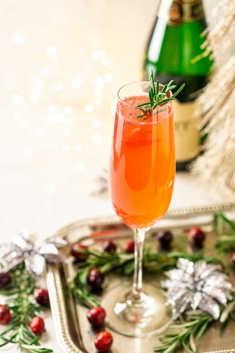 A cranberry French 75 on a silver platter with rosemary and cranberries around it.