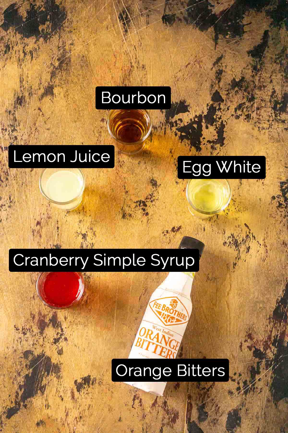 The cranberry bourbon sour ingredients with labels on a wooden board.
