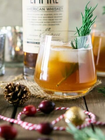 A cranberry bourbon smash with Christmas decor and a bottle of bourbon in the background.