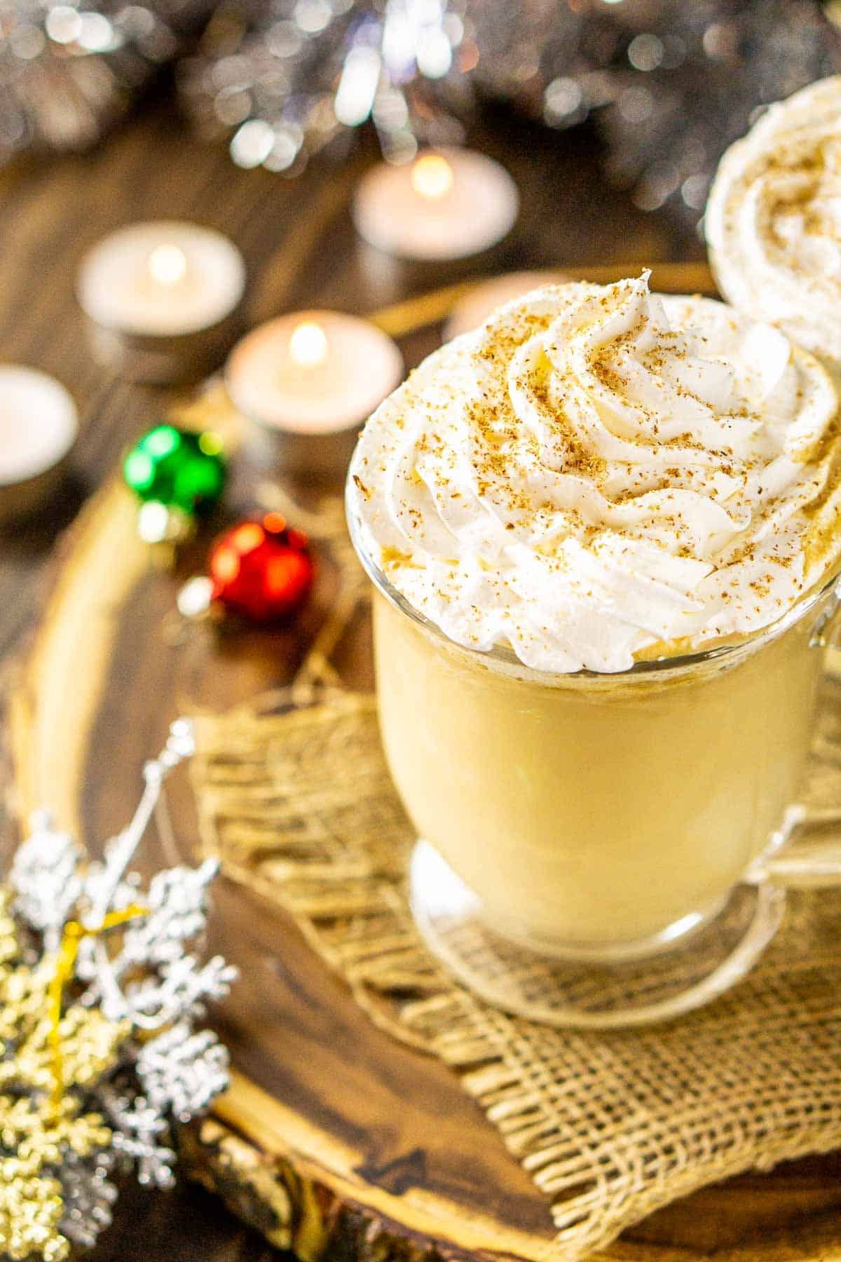 A close-up of an eggnog latte with Christmas ornaments and candles around it.