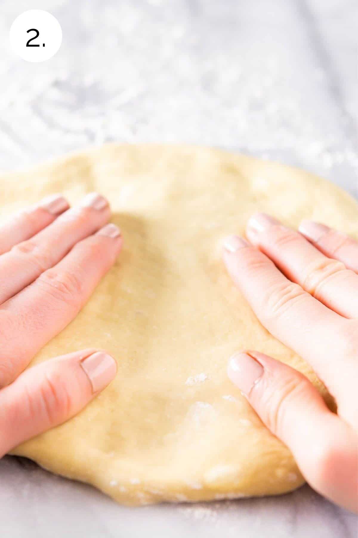 Patting the pizza dough with fingers on a countertop.