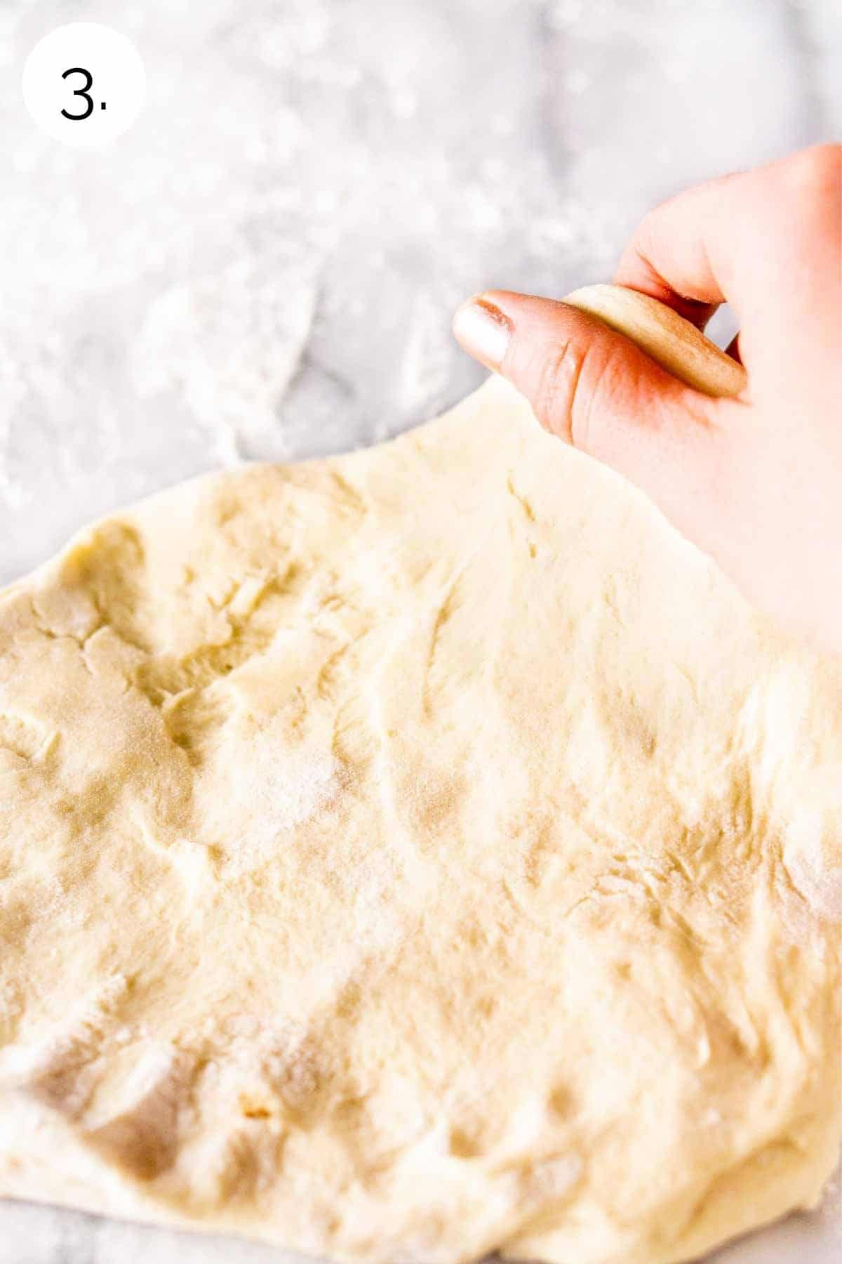 Hand stretching the pizza dough on a floured countertop.