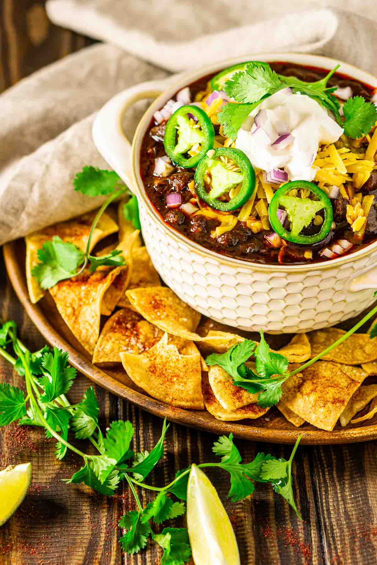 A bowl of short rib chili with chips and cilantro sprigs around it.