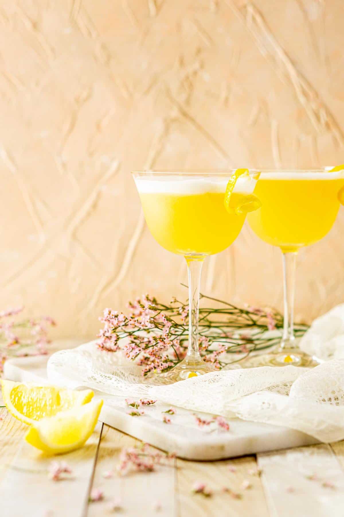 Two tequila sours on a marble board with purple flowers around them.