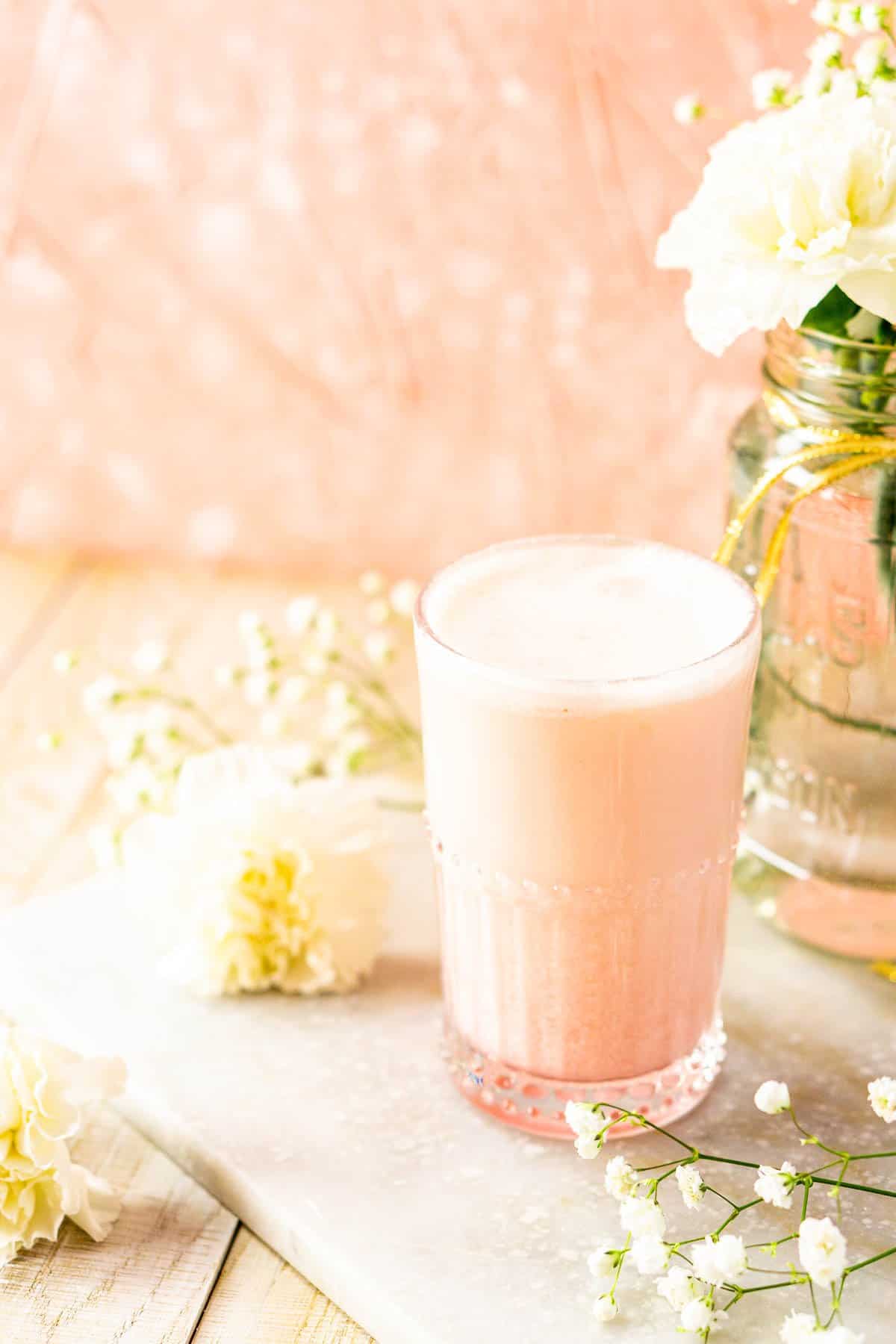 A blood orange gin fizz on a white board with flowers to the side.