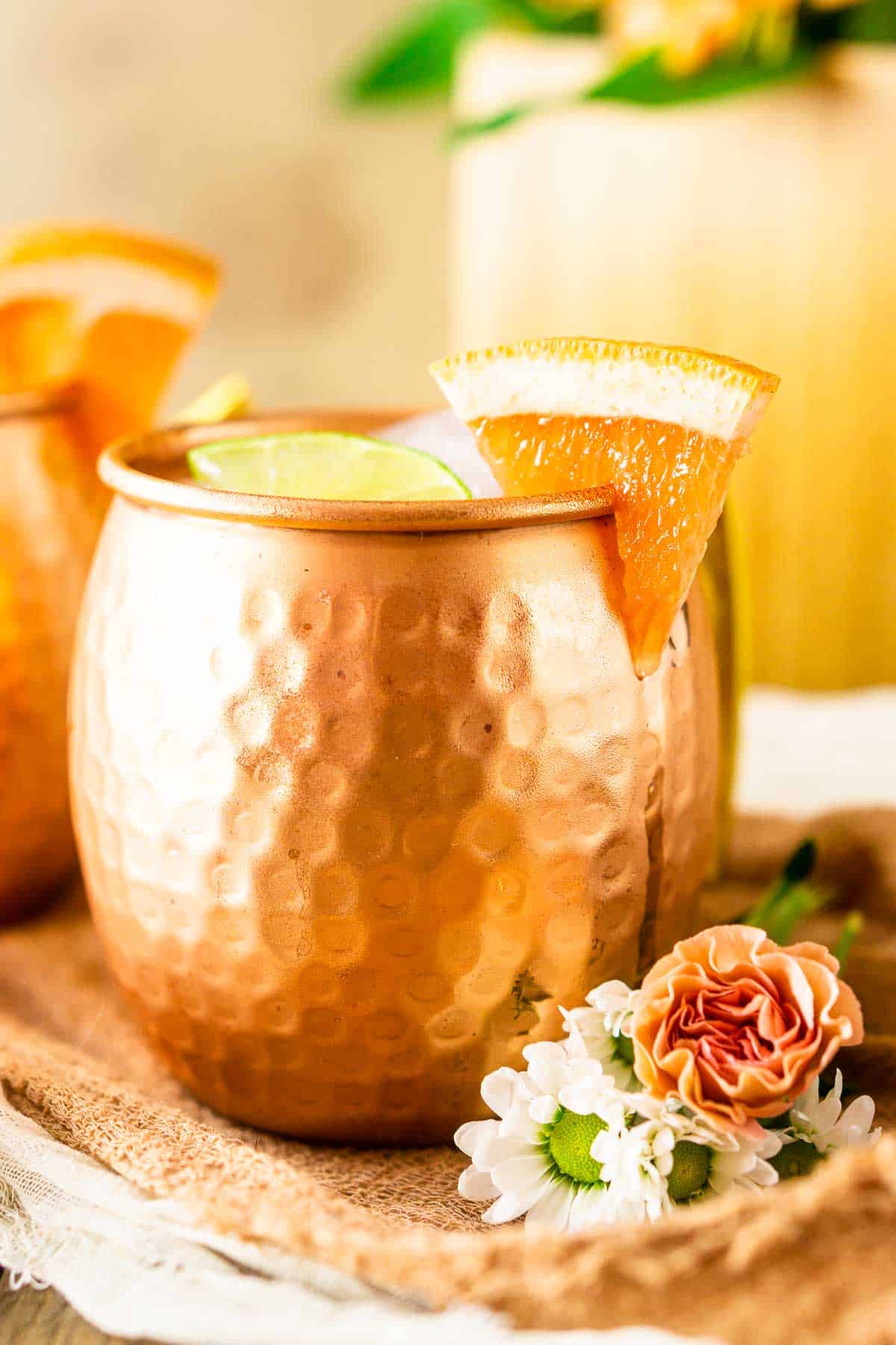 A grapefruit gin mule with pink and white flowers against the mug.