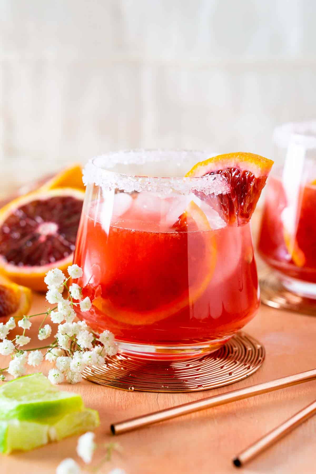 A blood orange margarita on a pink surface with flowers.