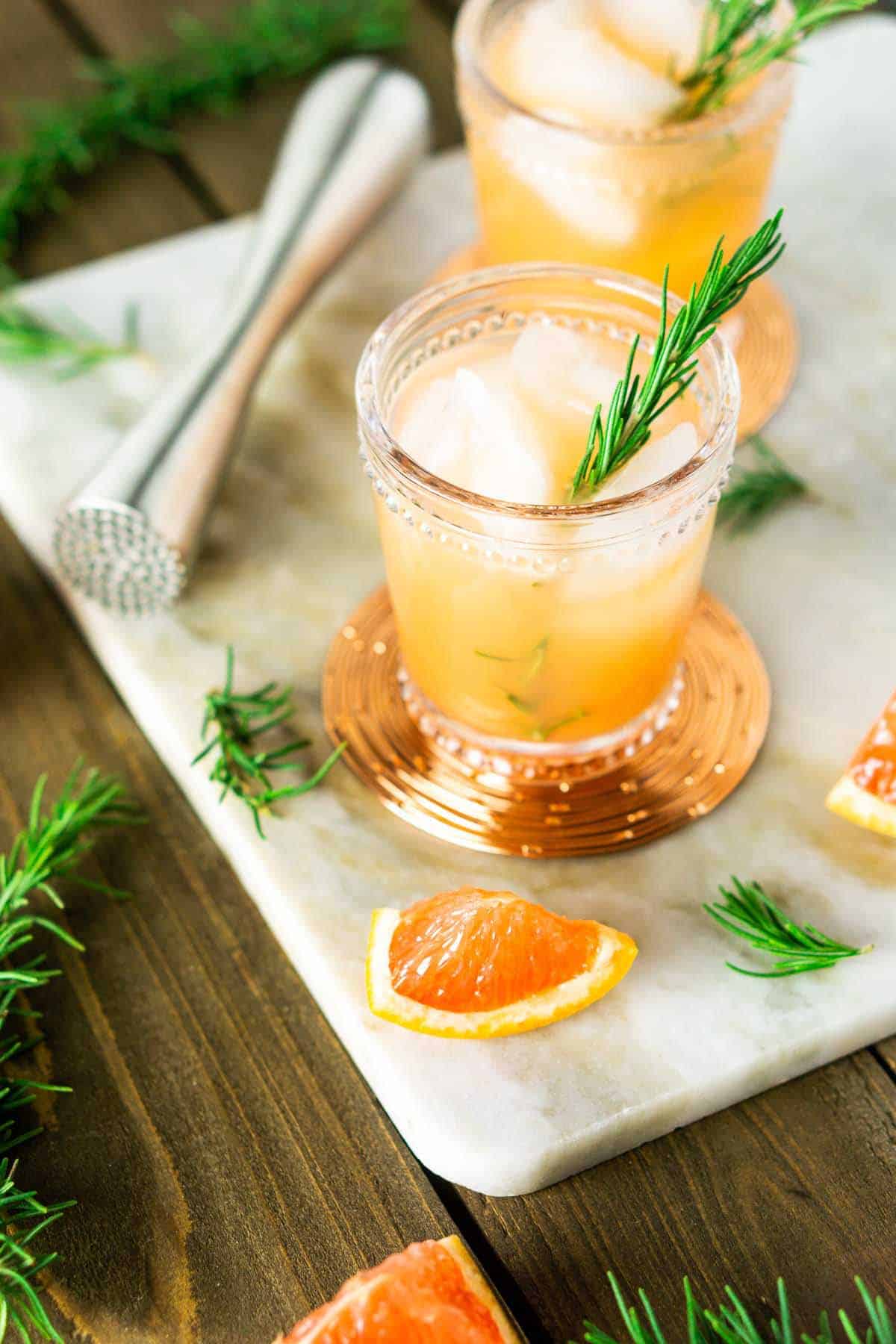 A rosemary-grapefruit vodka spritzer on a marble board with fresh herbs.