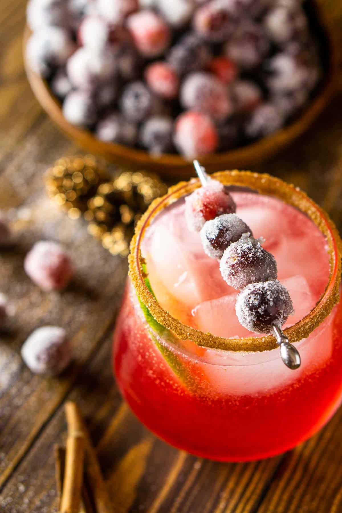 A cranberry margarita with sugared berries on a wooden plate behind it.