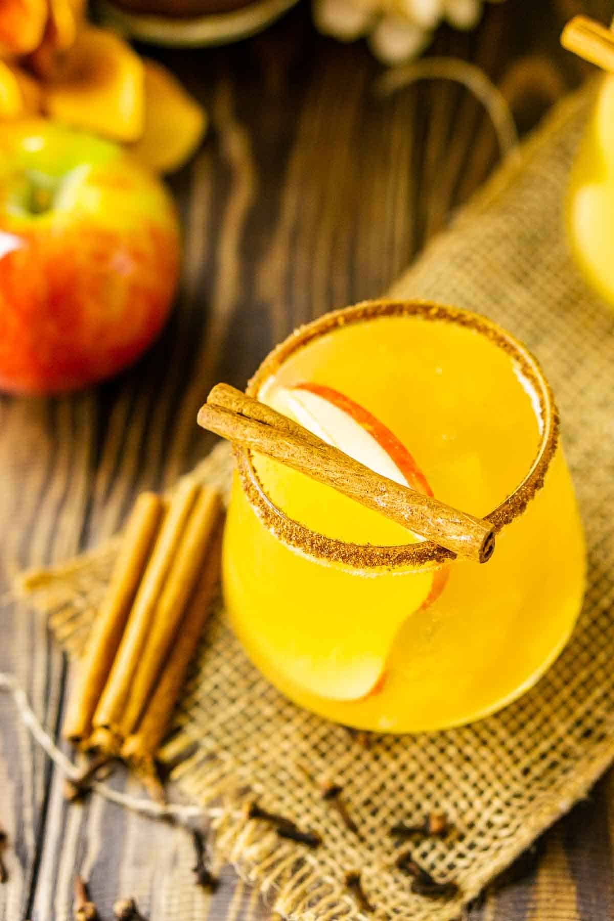 An apple cider cocktail on a piece of burlap with festive decor around it.