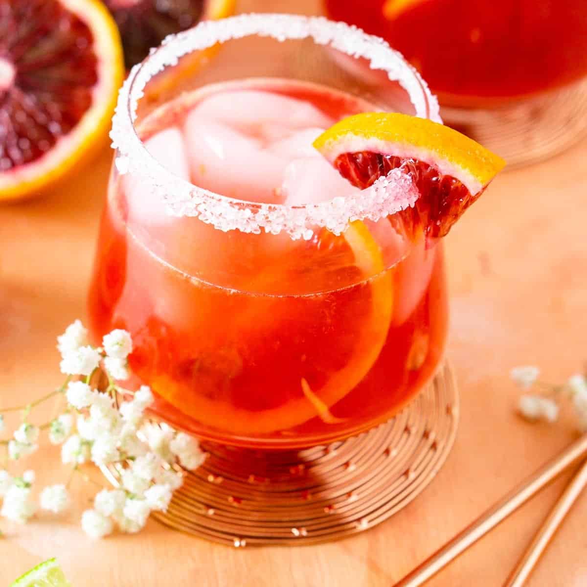A winter margarita with blood orange on a pink surface with flowers to the side.