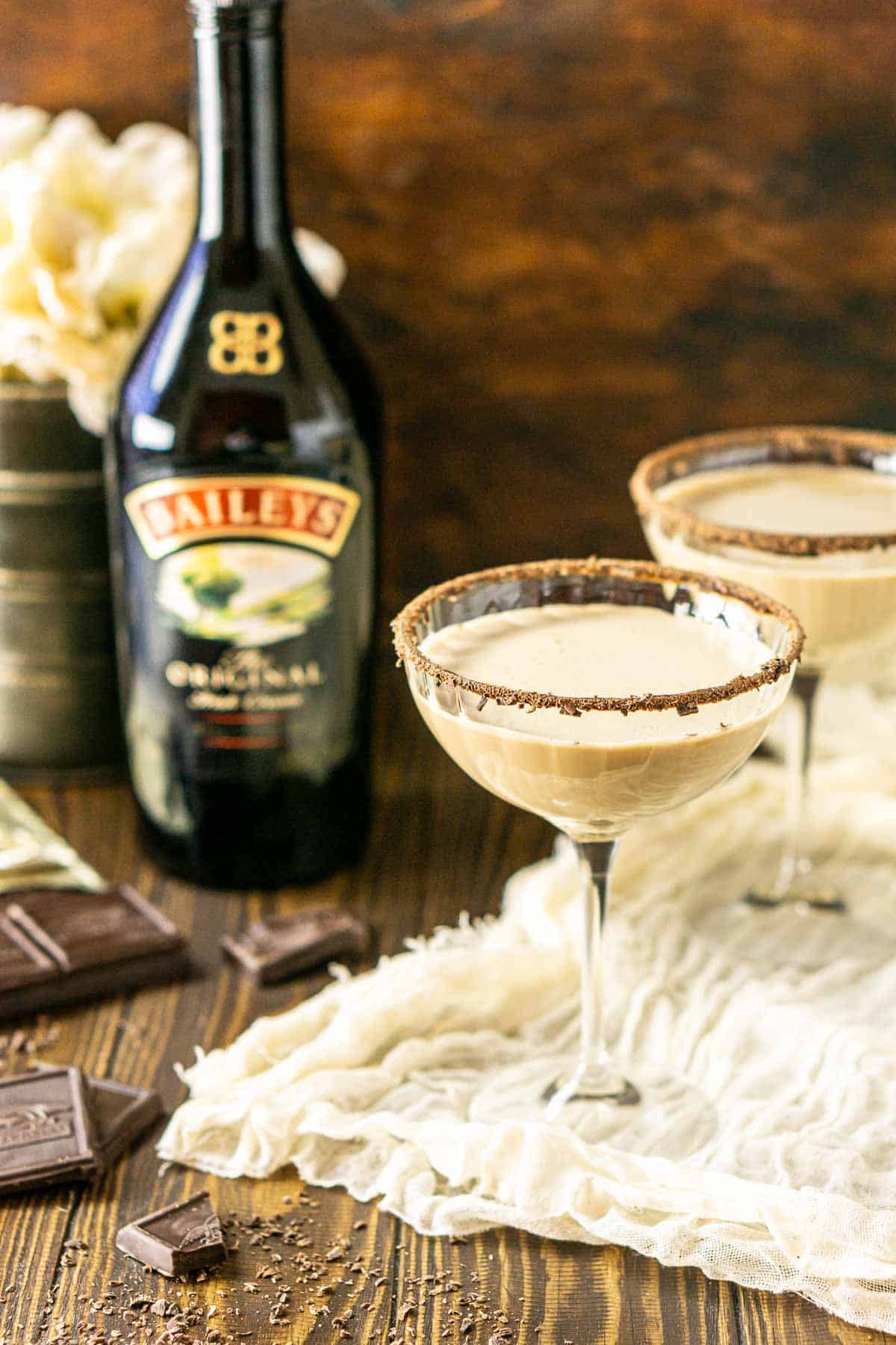 Two Baileys chocolate martinis with a bottle of Irish cream and chopped chocolate to the side.