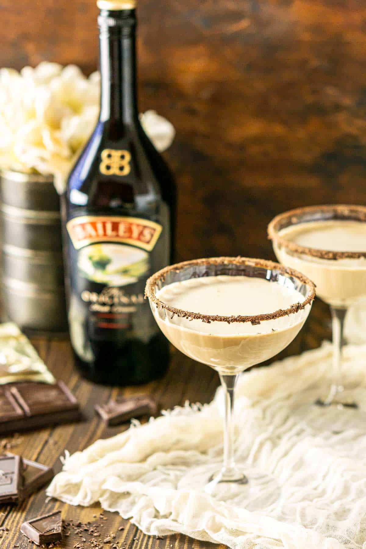 Two Baileys chocolate martinis with flowers and Irish cream behind them.