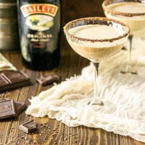 Two Baileys chocolate martinis with a bottle of Irish cream and chopped chocolate to the side.