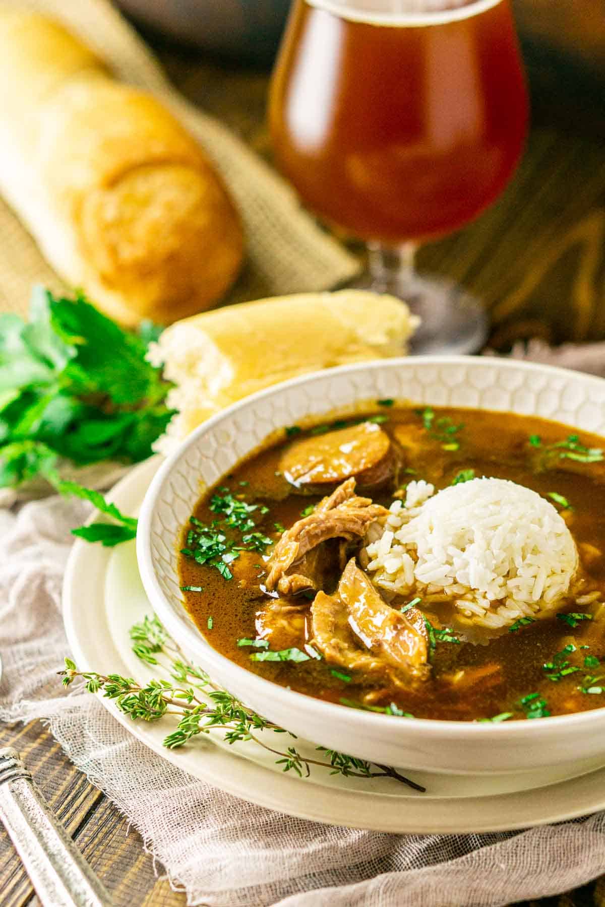 The duck gumbo on a plate with a beer and loaf of bread in the background.