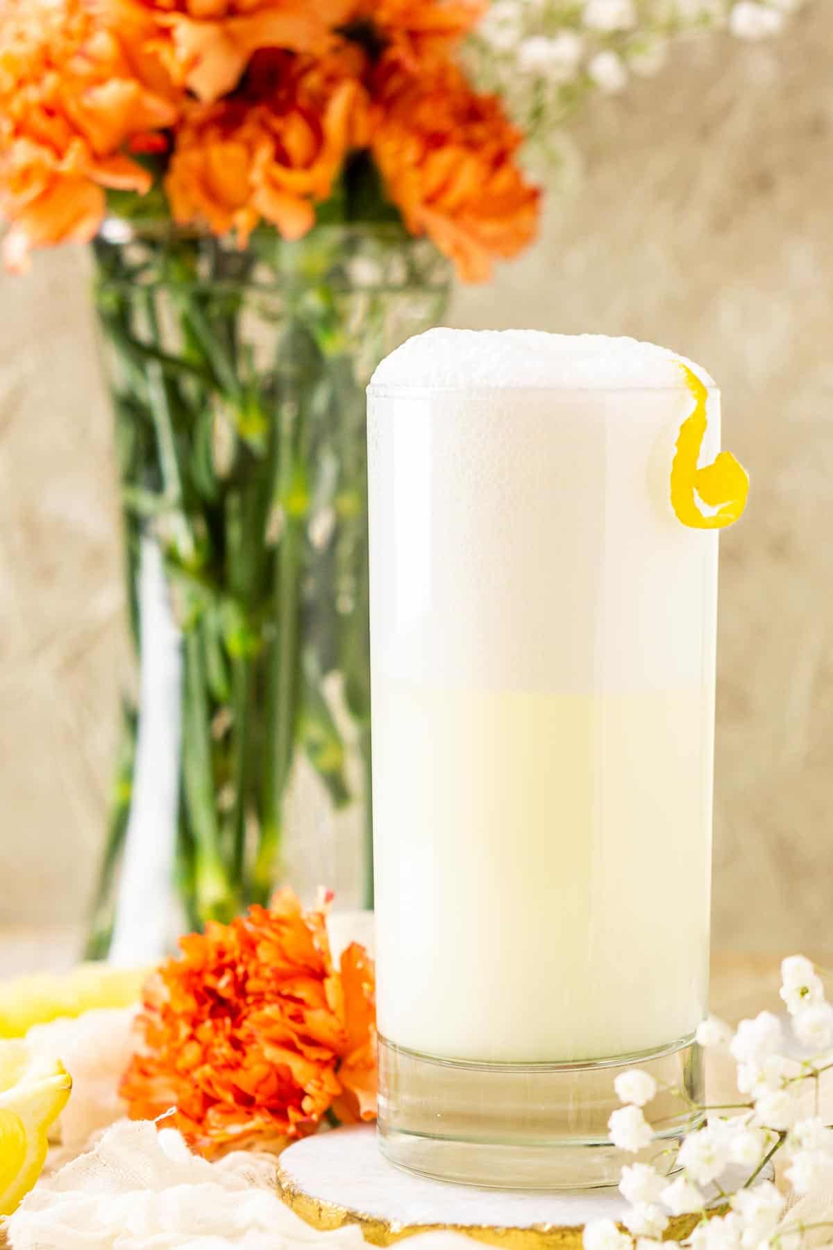 A close-up shot of a single New Orleans fizz with white and orange flowers framing the drink.